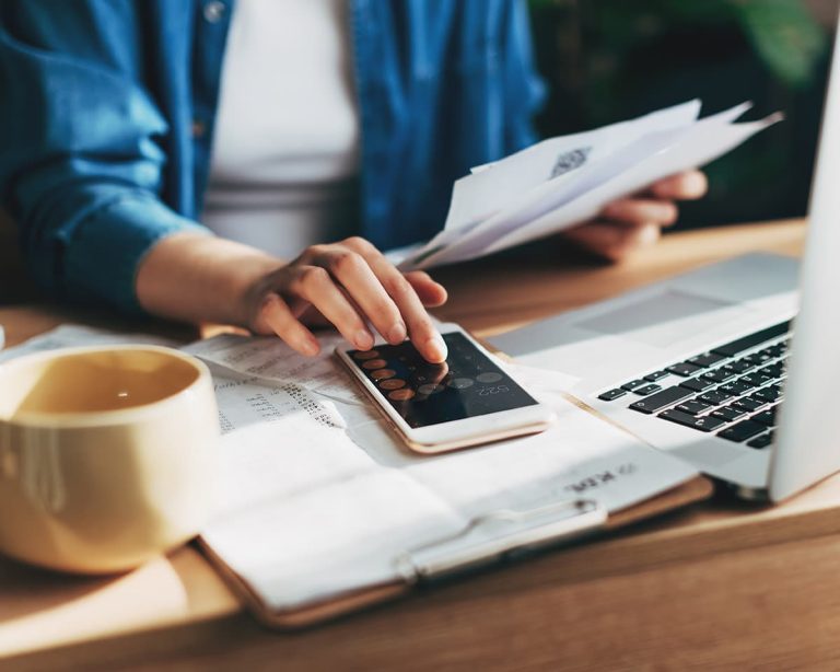 A woman using a calculator and reviewing documents on a work desk